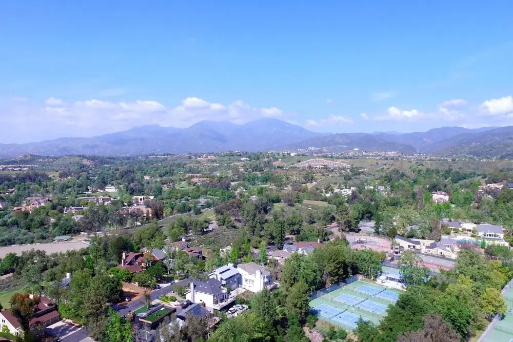 Aerial view of a wooded residential area with tennis courts and mountains behind