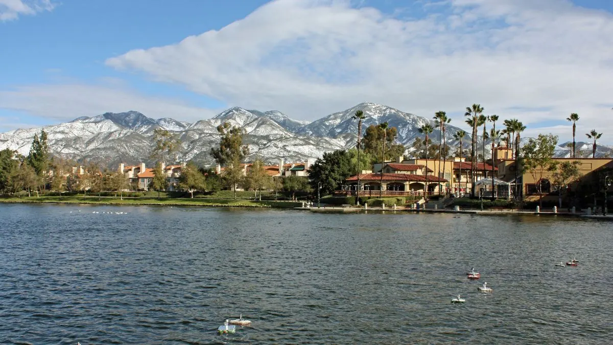 Lake with palm trees and homes along the shore, with snow-capped mountains behind