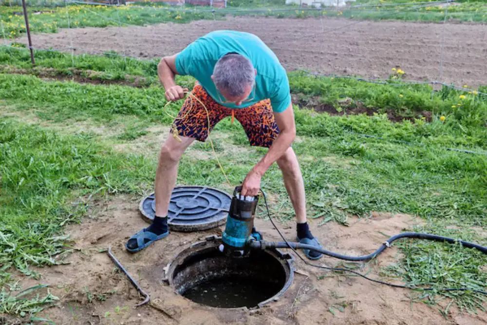 Person lowering a submersible pump into a sump pit in a field